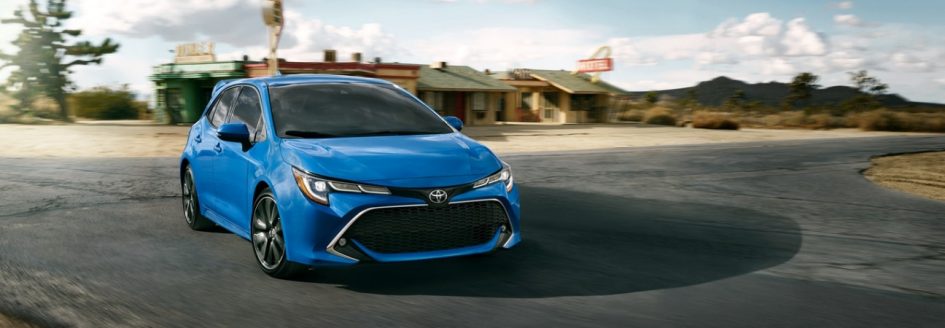 2019 Toyota Corolla Hatchback in blue rounding a paved corner along a desert road.